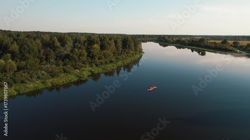Aerial view of two young girls paddling on SUP boards along river lined with green banks. Fast shooting. Paddleboard its great way to travel by water, rest and relaxation