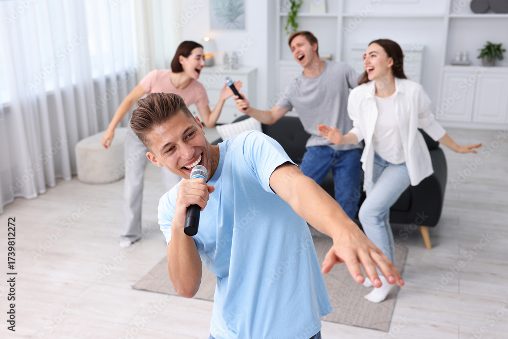 Obraz premium Young man singing karaoke with friends at home, selective focus
