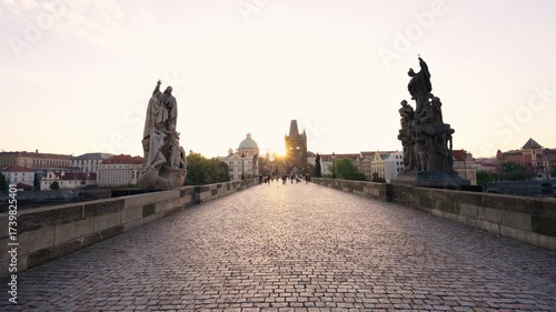 Stunning sunrise over Prague with warm golden light illuminating historic architecture, cobblestone streets, and iconic city landmarks in high-quality detail.