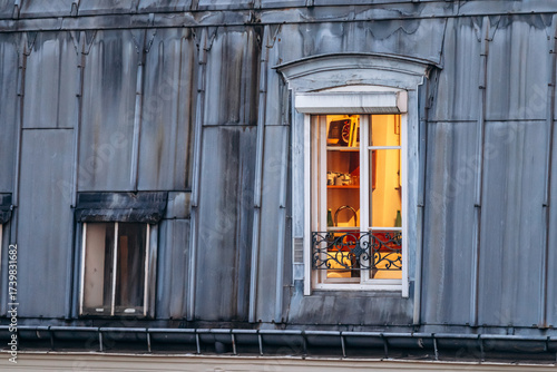 Photography Illuminated window of a Parisian mansard apartment, with warm light shining from