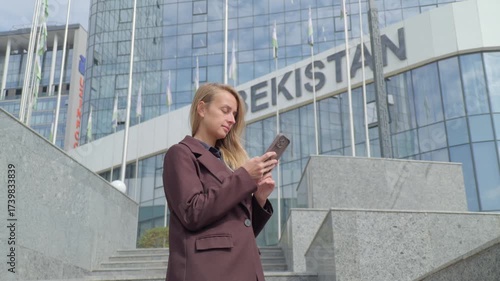 Young woman using smartphone near IT Park buildings and modern offices in Tashkent