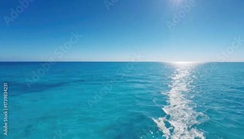 A vast expanse of turquoise ocean with a bright sun and wake.
