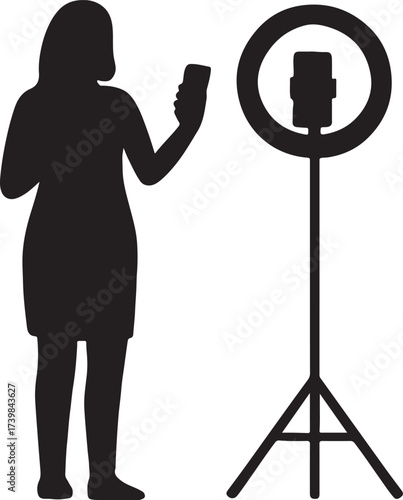 Silhouette of a woman holding a smartphone and recording a video with a ring light and tripod setup