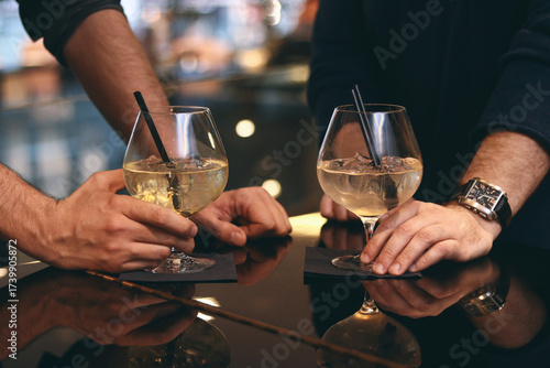 Photography Two people toasting with white wine spritzers or cocktails in elegant balloon glasses at a dark, upscale bar