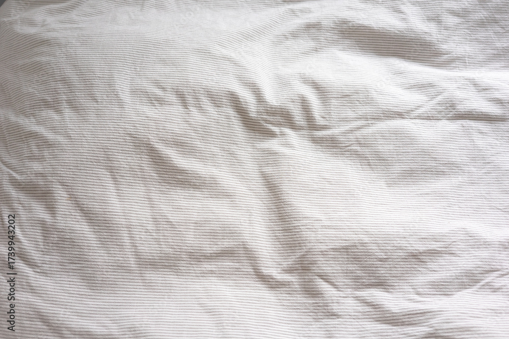 Naklejka premium Crumpled white fabric with fine striped pattern covers the surface. This minimal background evokes comfort, softness, and cozy home lifestyle themes.