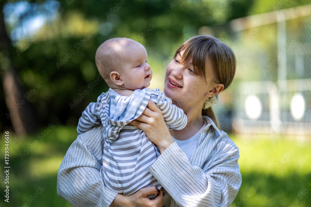 Fototapeta premium Bright portrait of happy mum holding infant child on hands. Loving mom carrying of her newborn baby.