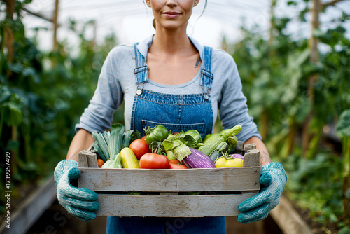A woman is holding a crate of vegetables in a greenhouse