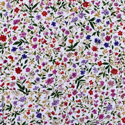 A dense floral pattern featuring an array of small, colorful blossoms & green leaves on white