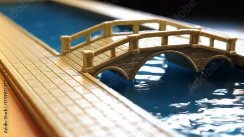 A detailed close-up of a miniature model featuring a small arched bridge over a bright blue canal.