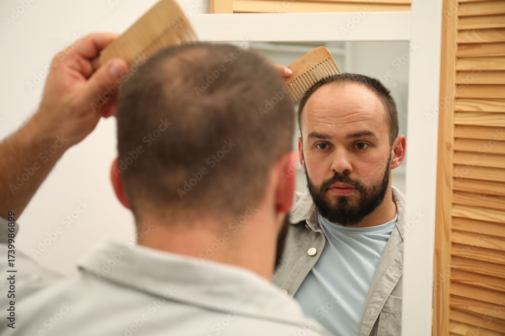 Fototapeta premium Baldness problem. Man brushing his hair with comb near mirror at home