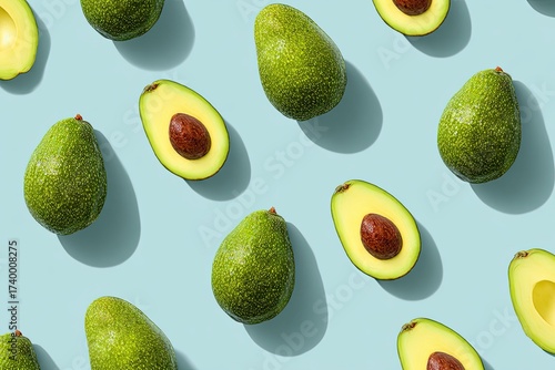 Overhead shot of numerous avocados, whole and halved, on a light blue background