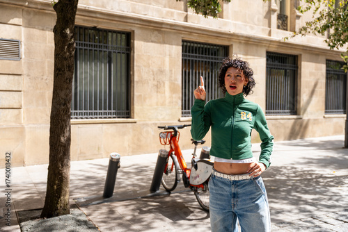 Young woman pointing upward near shared bicycle in urban setting