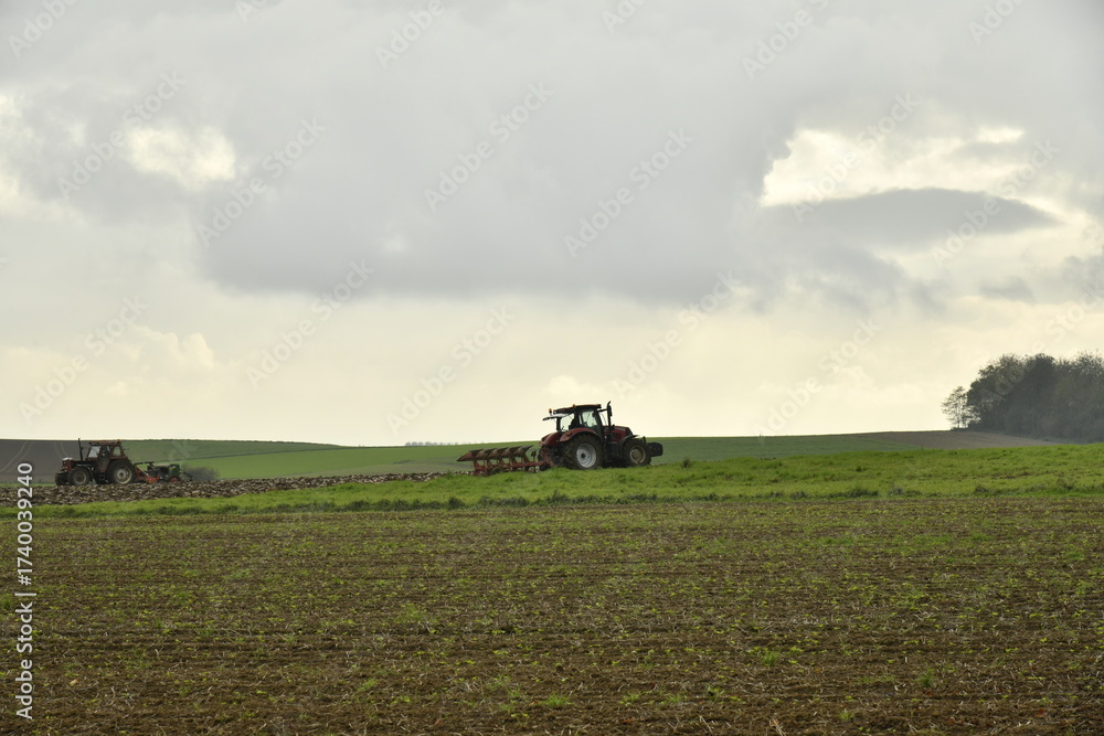 Obraz premium Tracteur labourant un champ sous les gros nuages gris en automne à Ghislenghien (Ath)