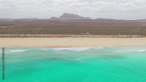 Aerial footage of Santa Monica Beach,showcasing endless white sand, turquoise waves, and a pristine,background volcanic mountain and desert,Boa Vista, Cape Verde.