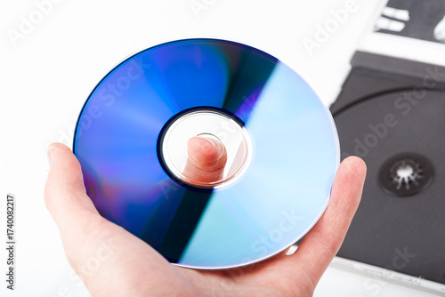 Hand holding a blue CD DVD optical disc with a right grip above an open cd case, reflective surface closeup detail, old data storage methods media concept, blank recordable disk up close, one person