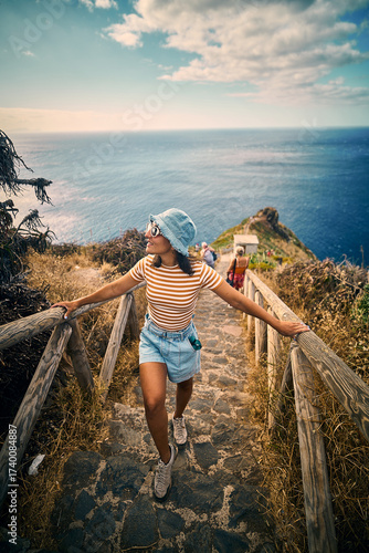 A young woman stands on the cliffs near the Cristo Rei statue in Madeira, Portugal, gazing toward the vast Atlantic Ocean.