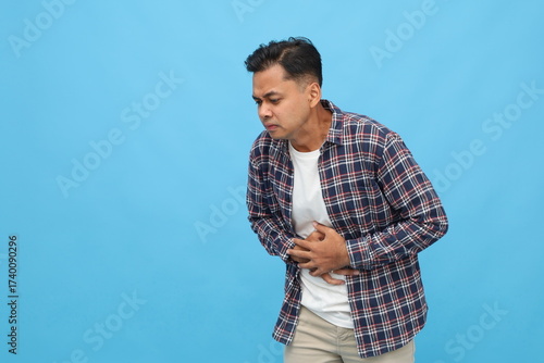 Young man experiencing stomach pain isolated on blue background with copy space.