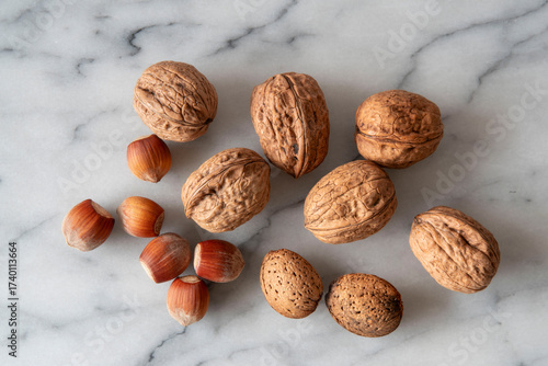 Close-up of almonds, walnuts and hazelnuts with their shells on white marble