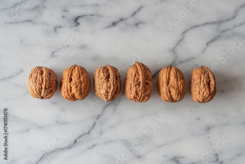 Close-up of walnuts in their shells lined up on white marble