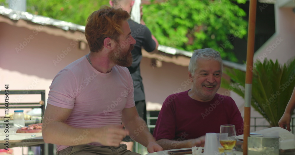 Naklejka premium Elderly man joyfully engaging with a younger man in an outdoor barbecue setting, smiling and dancing together in a moment of celebration and shared happiness