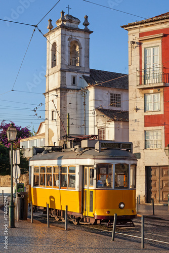 A classic fampus  yellow tram passes by vibrant red historic buildings in Lisbon  early sunrise morning