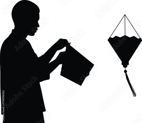 Silhouette of young person carefully folding paper to create origami lantern decoration with tassel, traditional craft activity symbolizing culture, creativity, and celebration