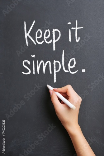 Hand writing with white chalk on a blackboard, showcasing the phrase Keep it simple, emphasizing clarity and simplicity in communication and expression