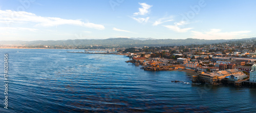 Photos Aerial view of Monterey, California, featuring the coastline, Cannery Row piers, calm Pacific Ocean waters, rolling hills, and scattered clouds