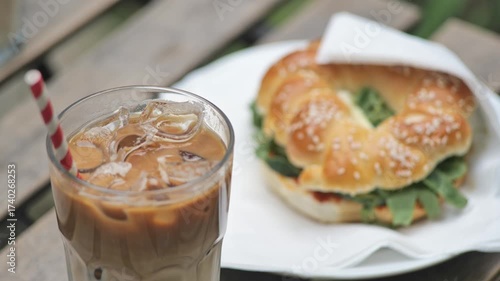 Ice coffee with paper straw and a bagel on a table outdoors cafe outside restaurant breakfast lunch simple food and drink concept, nobody.