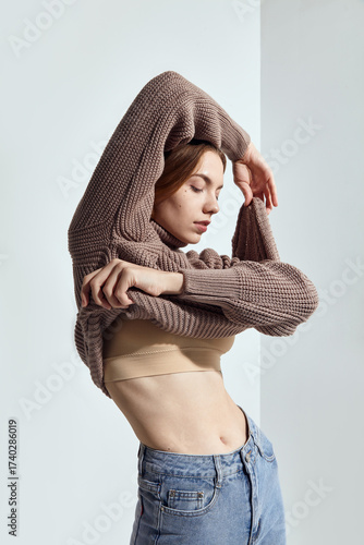 A beautiful woman in a beige knitted sweater poses on a gray background