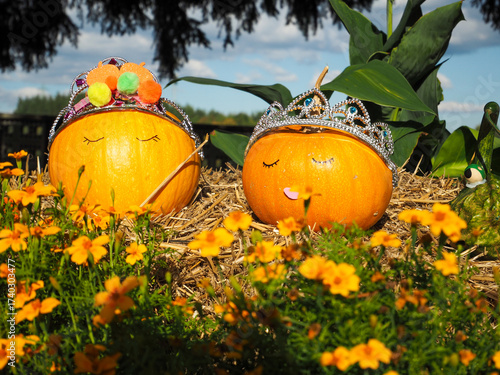 Two Small Decorative Pumpkins with Faces on Hay Bale — Autumn Scene with Flowers