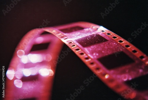 Close-up of a strip of film, curved against a dark background. Highlights gleam on the frames