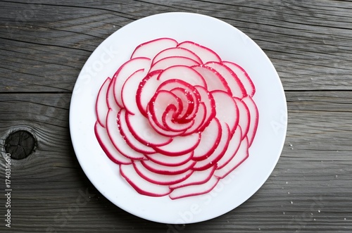 A vibrant plate of thinly sliced, spiral-cut radishes, lightly salted and presented as a simple, refreshing snack, perfectly complementing a cold beer.