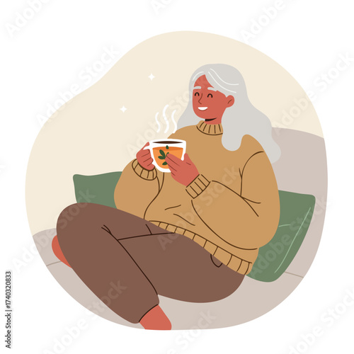 Elderly woman with grey hair sits comfortably, enjoying a warm cup of tea on a sofa