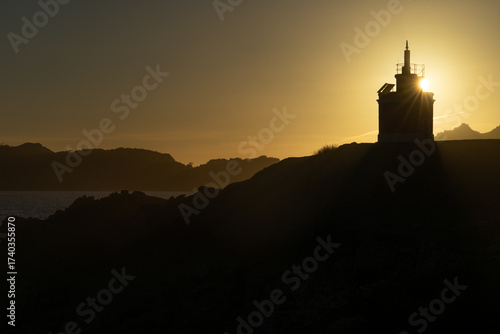 Punta Robaleira red lighthouse in Home cape at sunset in Rias Baixas zone in Galicia coast with Cíes islands in the background.