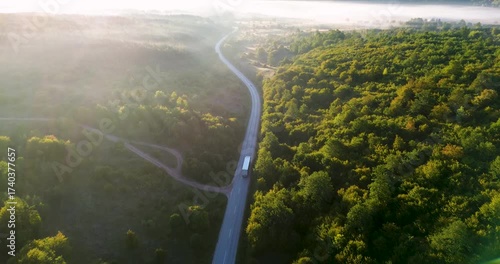 Aerial view of a truck driving on a foggy forest road at sunrise