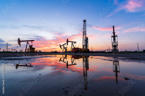 in the evening, oil pumps are running, The oil pump and the beautiful sunset reflected in the water, the silhouette of the beam pumping unit in the evening.