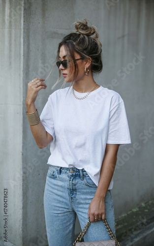 A fashion photography shot of a young woman wearing a casual white oversized t-shirt and light blue high-waisted jeans.