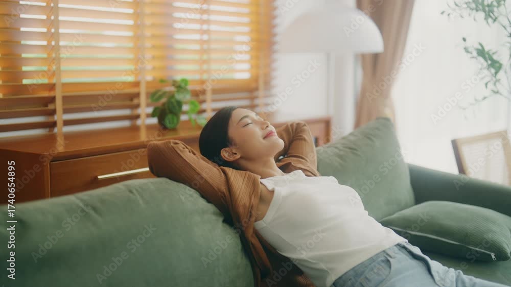 Relaxed young Asian woman enjoying rest on comfortable sofa, calm attractive girl relaxing on couch, breathing fresh air with eyes closed, meditating at home