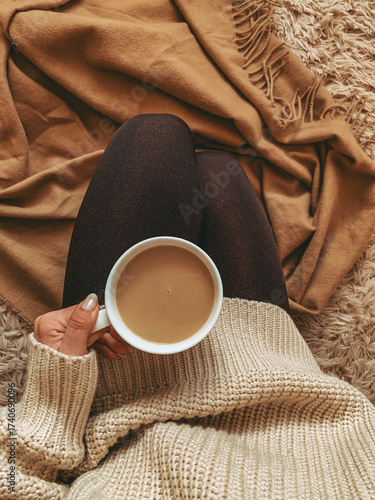 A woman in a sweater holds a cup of coffee