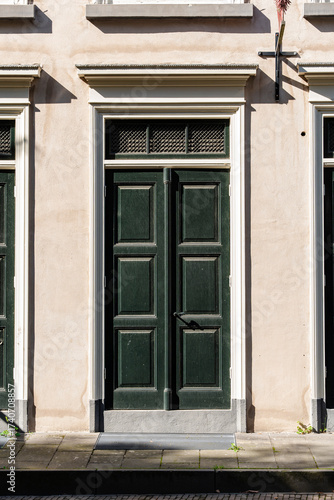 Ornate green wooden door set into a stucco building with white trim and a tiled vent above the entry.