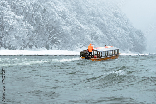 Winter Boat Journey on the Mogami River, Yamagata. A traditional wooden boat navigates the cold waters of the Mogami River surrounded by snow-covered forests in Yamagata, Japan