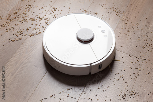 Smart robot vacuum cleaner removes scattered debris from the laminate floor.