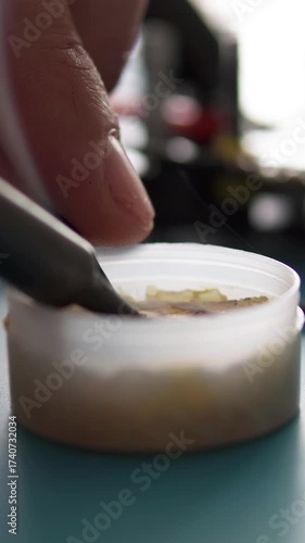 A specialist performs soldering on an FPV drone, attaching power and signal wires to its control board. Close-up of wires being tinned in rosin. Vertical video frame.