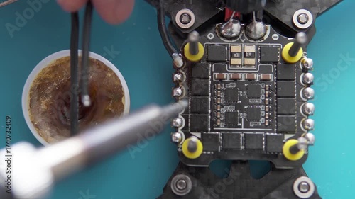 A specialist performs soldering on an FPV drone, attaching power and signal wires to its control board.	
