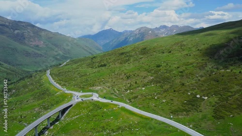 aerial footage showcasing a winding mountain pass road with a prominent roundabout, nestled amidst the lush green slopes of the Pyrenees mountains in Andorra under a beautiful sky.
