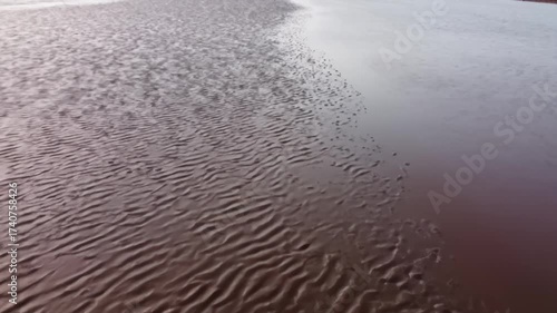 Serene tidal patterns where textured sand meets still water.