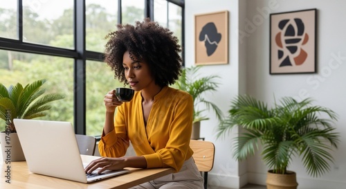 Focused african american woman drinking coffee while using a laptop for remote work from home