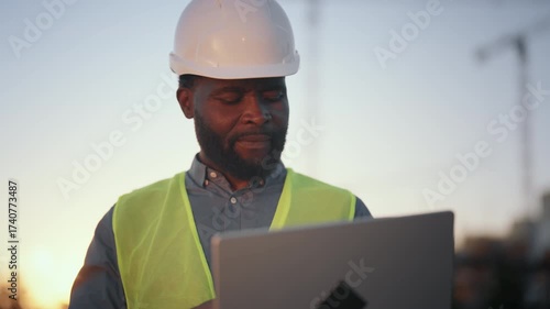 Medium portrait of high-skilled engineer with laptop at construction site. Innovation and modern technology in architecture and development, new software for builders and foreman, african american man