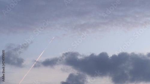 A clear sky with soft clouds and a visible contrail. The scene captures the tranquility of nature and the impact of human activity in the atmosphere.